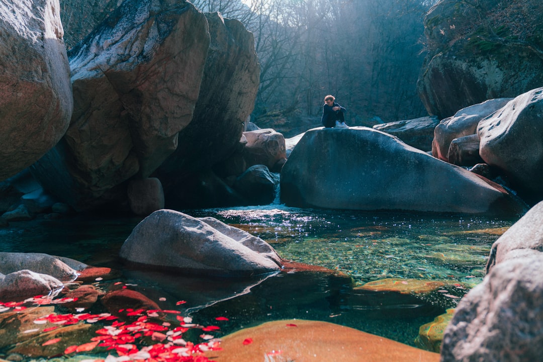 man in black jacket sitting on rock near river during daytime