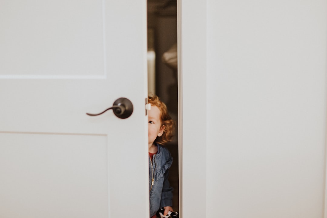 A little girl peeking out from behind a door
